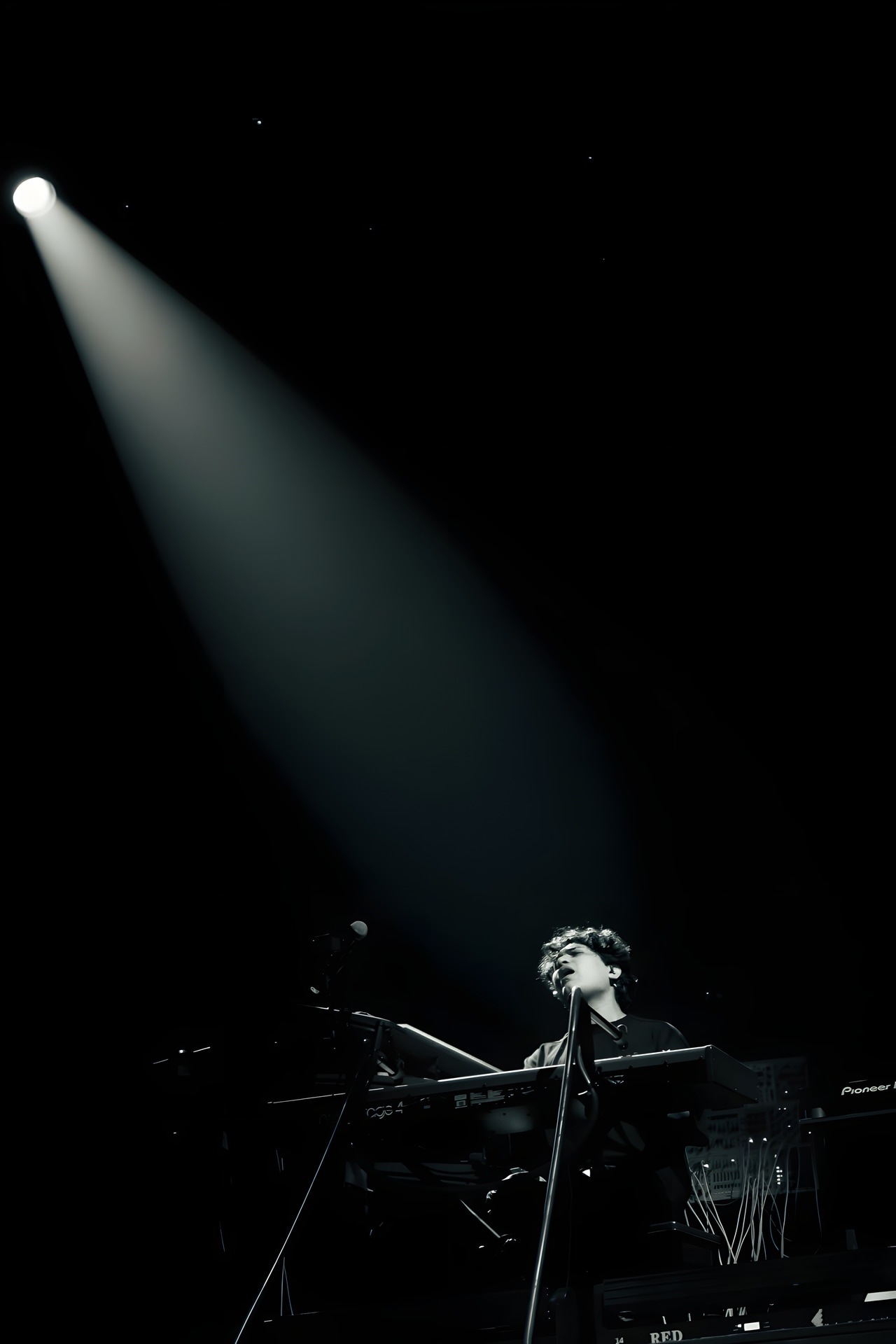 A white spotlight falls through darkness onto Shashwat Sachdev at the keyboards.